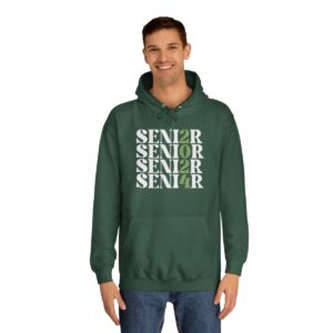 A smiling man wearing a green hoodie with the word "SENIOR" printed in a vertical column in different sizes and a pair of blue jeans.