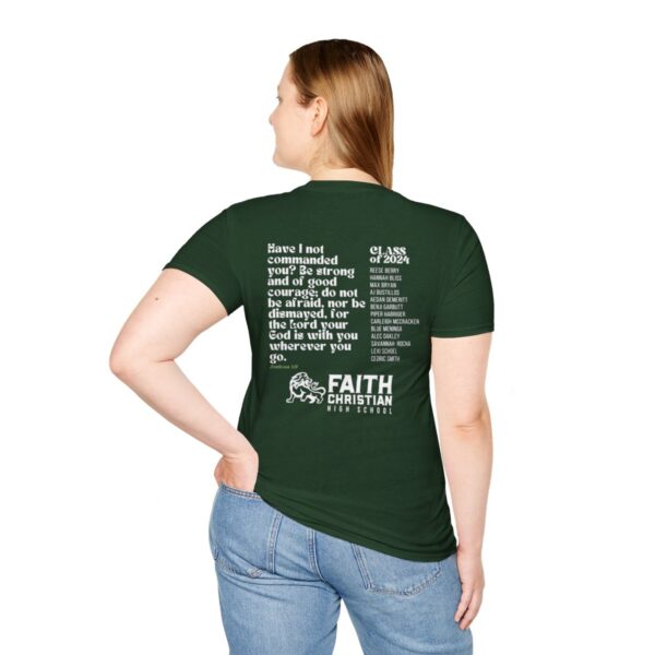 A woman standing with her back to the camera wearing a green t-shirt with white text that includes a religious quote, a school mascot logo for Faith Christian High School, and a list of names from the class of 2024. She is wearing blue jeans and has her hands partially tucked into the pockets.