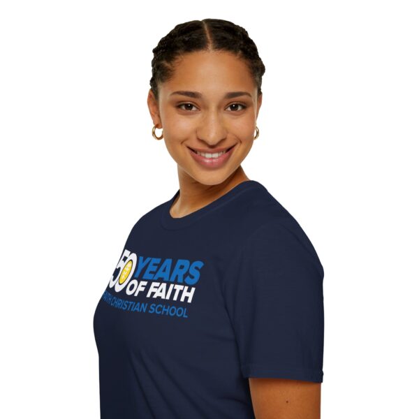 A smiling person with hoop earrings and braided hair wearing a blue T-shirt that reads "50 YEARS OF FAITH CHRISTIAN SCHOOL" on a plain background.