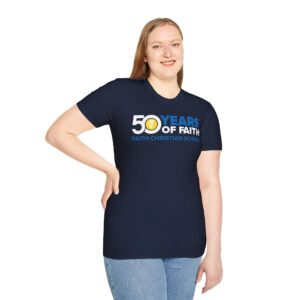 A woman standing with one hand on her hip, wearing a dark blue t-shirt with the inscription "50 YEARS OF FAITH, FAITH CHRISTIAN SCHOOL" and light blue jeans.